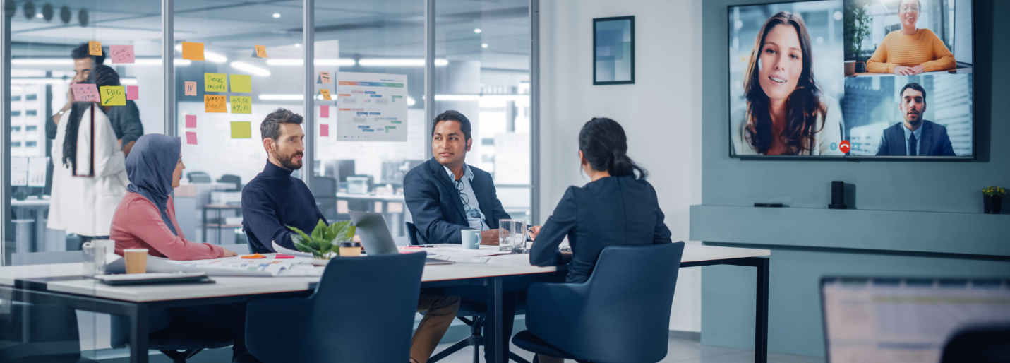 Group of coworkers in office and on large conference room screen show virtual SAP project management agency meetings.